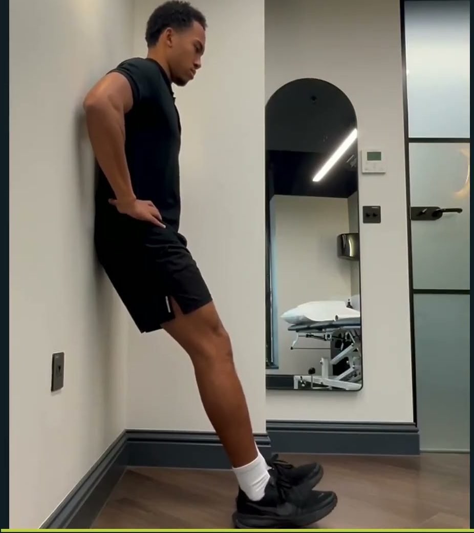 Otis, physiotherapist at BOOST PHYSIO West Hampstead, demonstrating a tibialis anterior toe raise against the wall